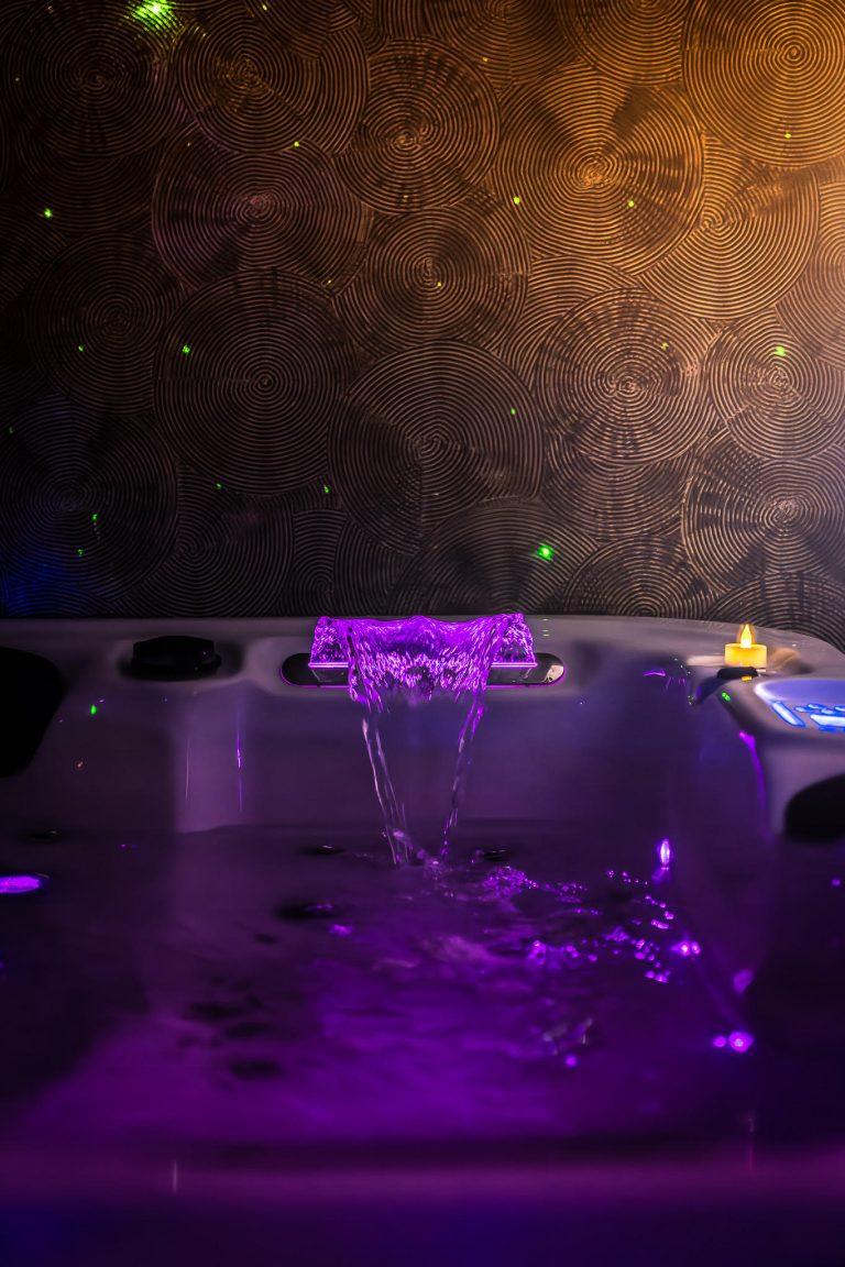 Jacuzzi intérieur avec sa cascade illuminée d'une violet éclatant.