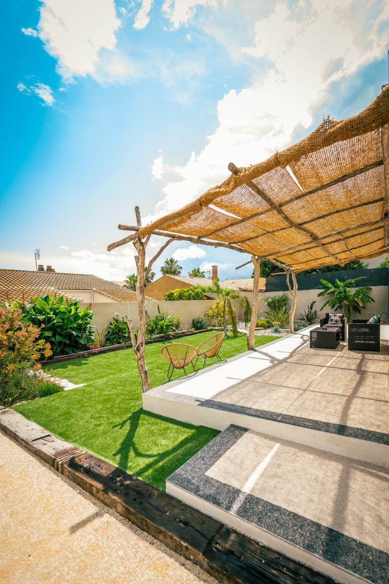 Terrasse un sud pour profiter du soleil en occitanie avec sa pergola en bois flotté,entourée de plantes verdoyantes et mobilier de jardin confortable,idéal pour un moment de détente en plein air.