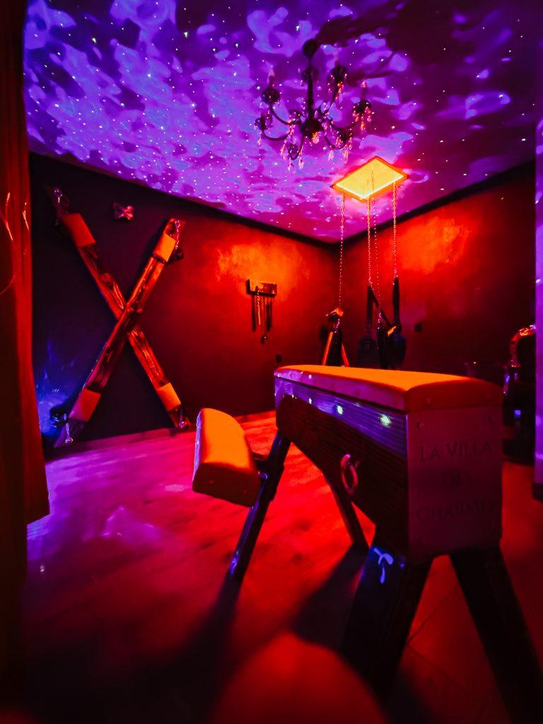 Secret room de luxe avec mobilier bdsm haut de game,ambiance tamisé et éclairage coloré sensuel.